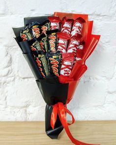 a bouquet of candy wrapped in black paper and tied with red ribbon on a wooden table