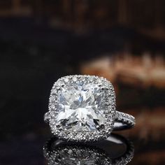 an engagement ring with a cushion cut diamond surrounded by pave diamonds on a reflective surface