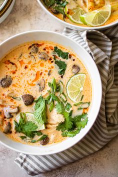 two bowls filled with soup and garnished with cilantro, parsley and lime