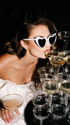 a woman wearing heart shaped glasses drinking champagne from a wine goblet on a tray