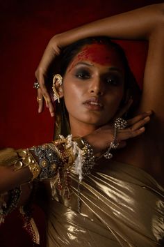 a woman with her hands on her head, wearing gold and silver jewelry while posing for the camera