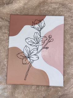 a pink and white painting with some flowers on it's side, sitting on a bed