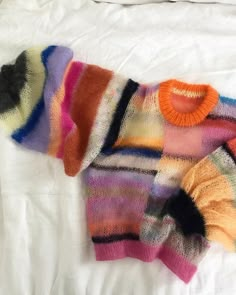 a multicolored sweater laying on top of a white bed next to a pillow