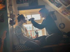 two people sitting in a room with guitars on the wall and one person cutting another's hair