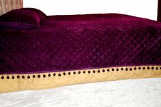 a bed with a purple comforter on top of it next to a red headboard