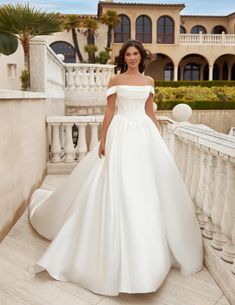 a woman in a white wedding dress standing on a balcony next to a large building