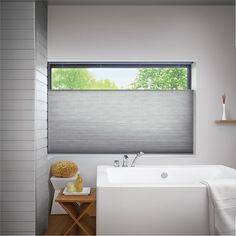 a white bath tub sitting under a window next to a wooden table with a vase on it