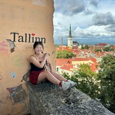 a woman sitting on top of a stone wall next to a building with graffiti written on it