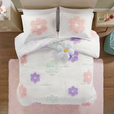 a white bed with pink and purple flowers on the comforter, along with two pillows