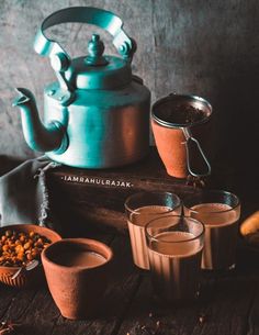 there are three glasses with drinks next to a teapot and some bananas on the table