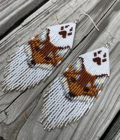 the beaded earrings are decorated with brown and white dog images on them, hanging from wooden planks