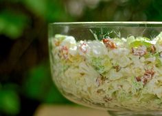 a glass bowl filled with coleslaw salad on top of a wooden table next to green leaves