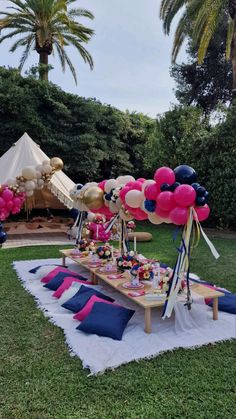 a picnic table with balloons and other items on it in the grass near some trees