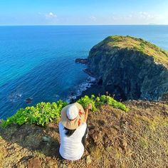 a woman sitting on top of a cliff next to the ocean