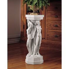 a white marble statue with a plant in the corner and wood flooring behind it