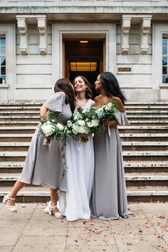 three bridesmaids standing in front of a building with their arms around each other