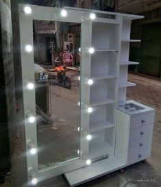 a white lighted vanity mirror with drawers and lights on the sides, in front of a building