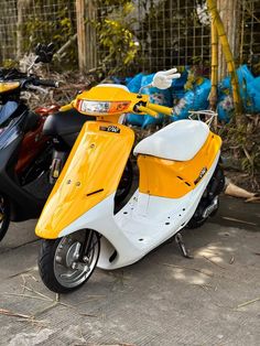 two motorcycles parked next to each other in front of a fenced area with trees