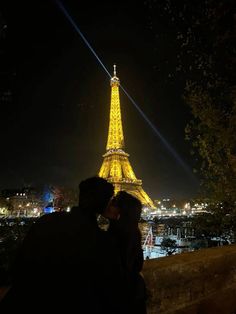 two people standing in front of the eiffel tower at night with lights on