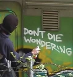 a man in a black hoodie writing on a green wall