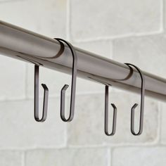 three hooks are hanging from the side of a metal rail on a white brick wall