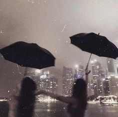 two people holding umbrellas in front of a cityscape at night with rain falling on them