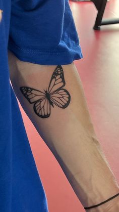 a person with a butterfly tattoo on their arm and wrist, standing in front of a pink floor