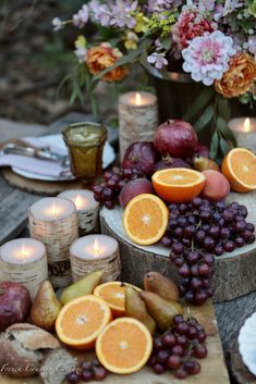 an assortment of fruits and candles on a wooden table with flowers in the back ground