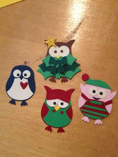 paper owls are sitting on the table with christmas decorations in front of them, and one owl is holding a star