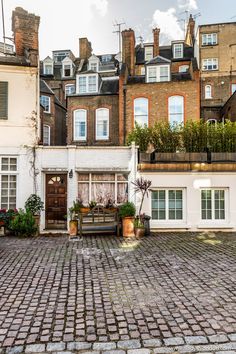 an old brick street with lots of buildings in the background and potted plants on either side