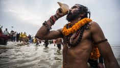 a man with dreadlocks drinking from a bottle in front of other people on the beach