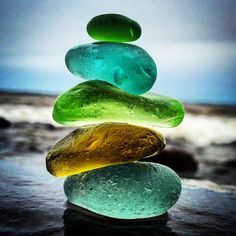 a stack of colorful rocks sitting on top of a wet beach next to the ocean