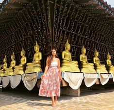 a woman standing in front of a row of golden buddhas on display at a temple