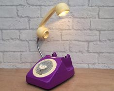 an old fashioned purple telephone sitting on top of a wooden table next to a brick wall