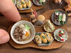 miniature food items displayed on wooden platter with fingernails and fingers pointing at them