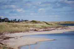 an empty beach with houses in the background and water running through it on a sunny day