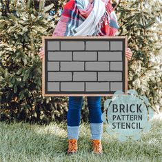 a woman holding a brick pattern stencil in front of a bush and trees