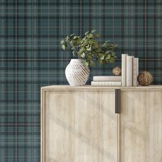 a wooden cabinet with books and a vase on it next to a plaid wallpaper