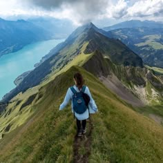 a person walking up a grassy hill with mountains in the background and water on the other side