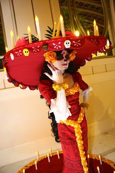 a woman dressed in red and yellow is holding a large hat with skulls on it