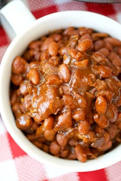 a white bowl filled with baked beans on top of a red and white checkered table cloth