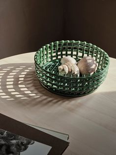 a green basket sitting on top of a wooden table next to a book and some shells