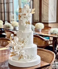 a wedding cake with white flowers on top is sitting on a table in front of chairs