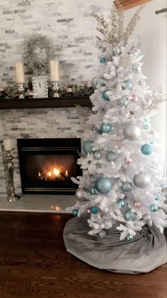 a white christmas tree with blue and silver ornaments in front of a fireplace decorated for christmas