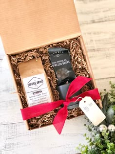 an open box with coffee and chocolates in it on a white wooden table next to greenery