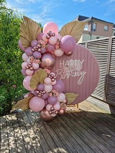 a happy birthday sign made out of balloons with leaves and flowers on it in the shape of a heart