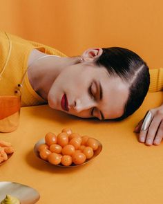 a woman laying her head on the table next to some oranges and other food