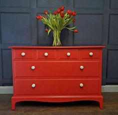 a red dresser with white knobs and tulips in the bottom drawer, against a blue wall