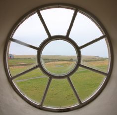 a round window in the side of a building with grass and fields seen through it