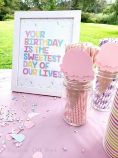 a pink table topped with lots of cupcakes next to a jar filled with candy